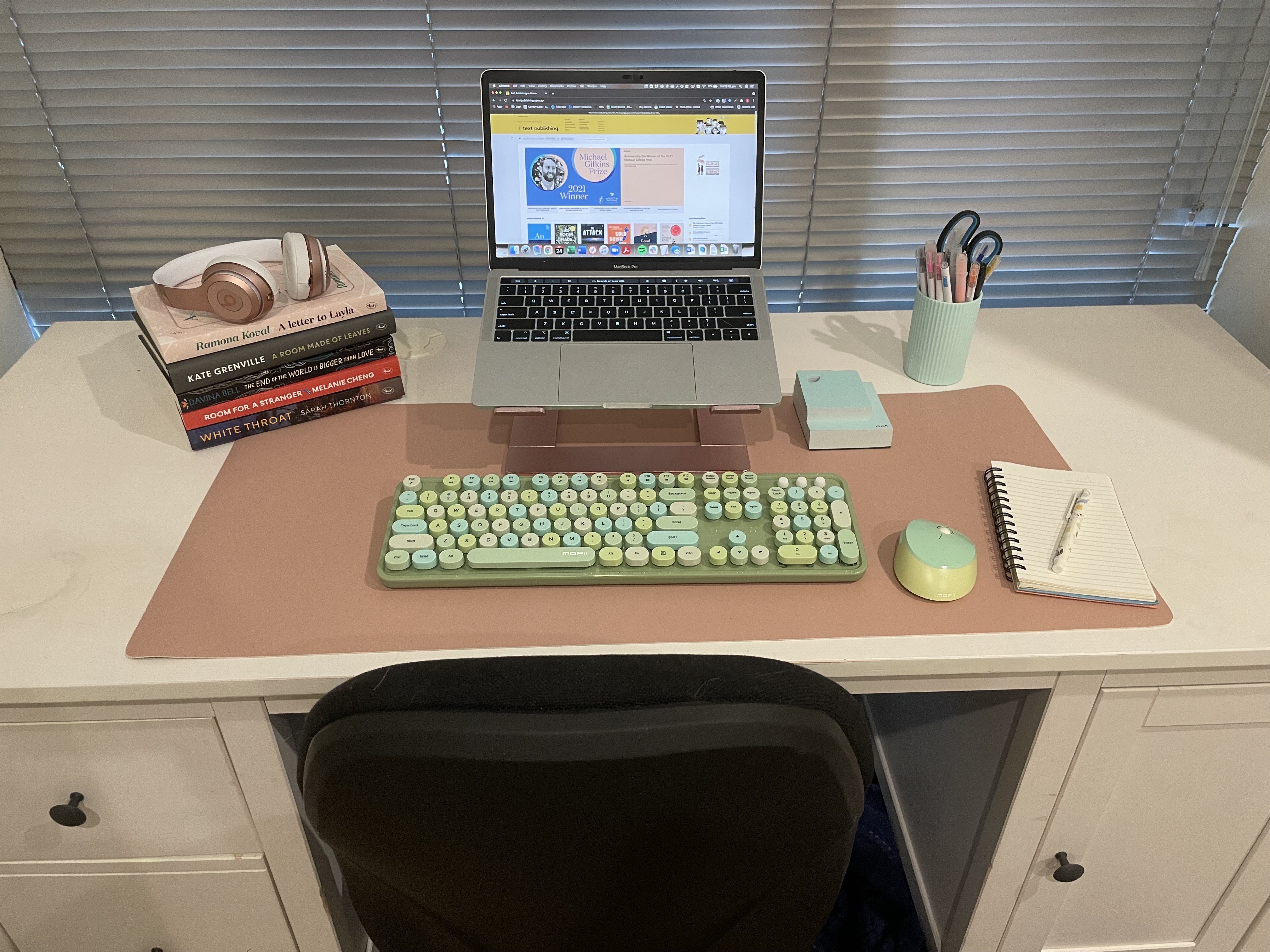 Sophie Mannix's desk: A laptop, a pen cup, a notebook, overear headphones resting on a stack of books, a keyboard and mouse.