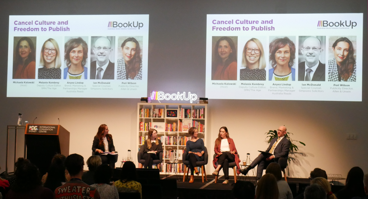 A photograph of four women and a man, sitting in chairs on the BookUp stage. Projected twice onto the wall behind them is a slide reading 'Cancel Culture and Freedom to Publish' above headshots of the speakers.