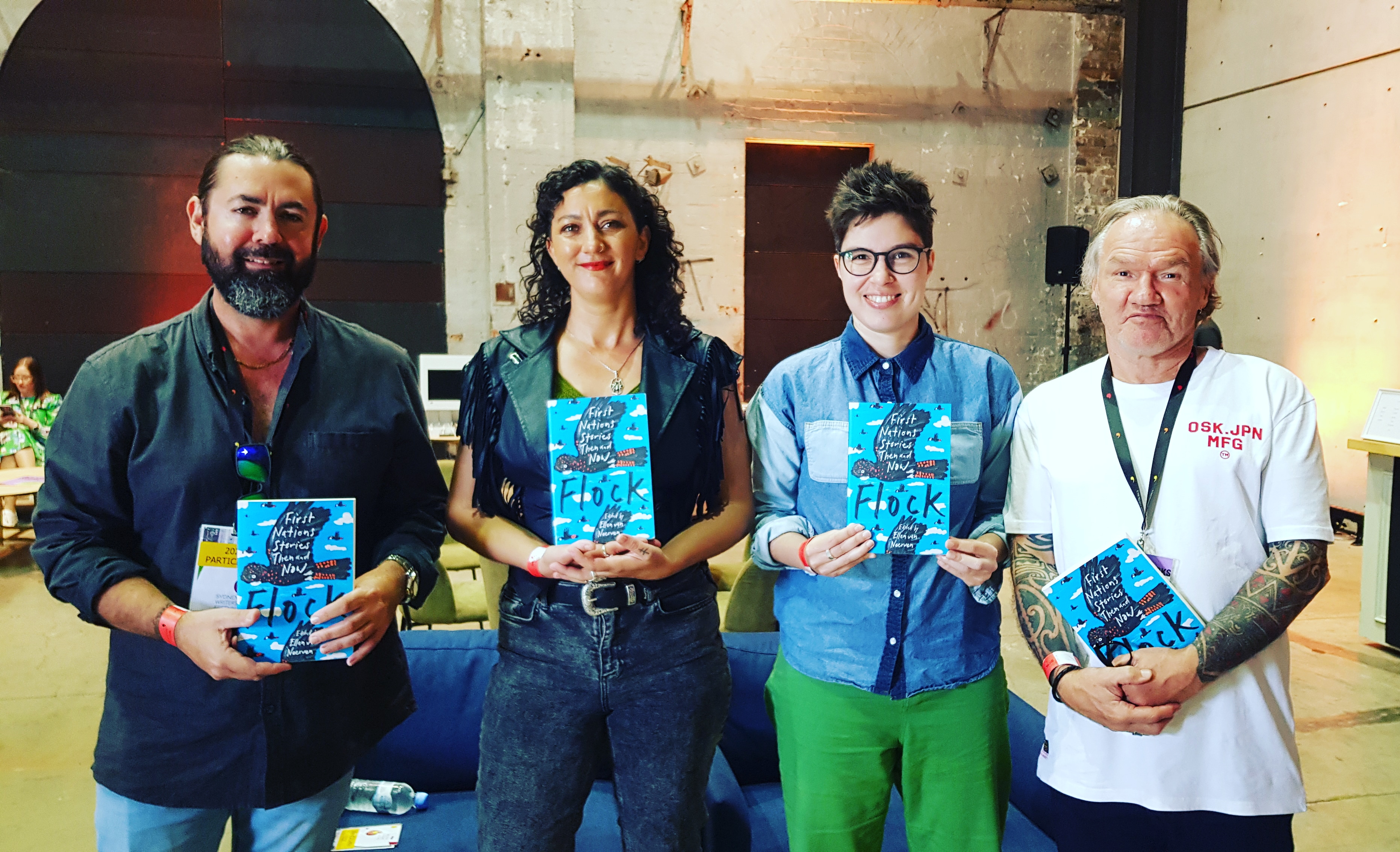 UQP authors Adam Thompson, Mykaela Saunders, Ellen van Neerven and Tony Birch pose with copies of Flock: First Nations Stories Then and Now. The anthology has a blue cover, with a sihlouette of a bird in flight.
